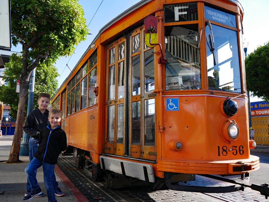 zwei-kinder-stehen-vor-historischer-orangener-strassenbahn-in-san-francisco