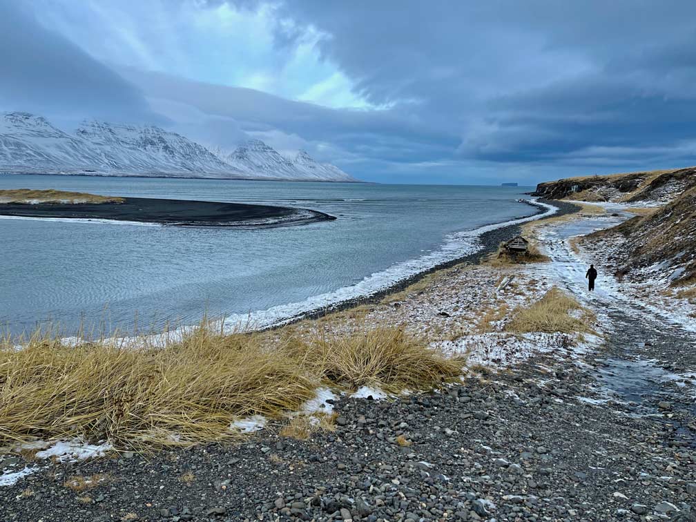 kind-laeuft-auf-schwarzen-sandstrand-am-meer-in-winterlicher-landschaft-zu