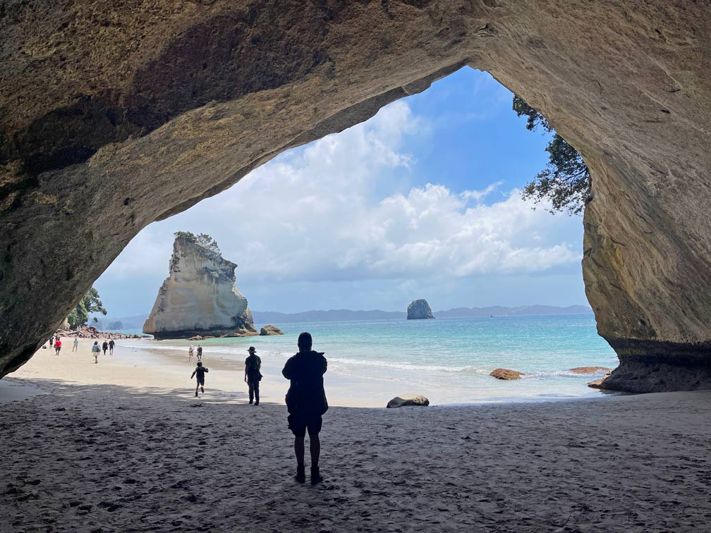 blick-aus-der-felshoehle-cathedral-cove-in-neuseeland-auf-den-strand-das-hellblaue-meer-und-einen-grossen-kalkstein