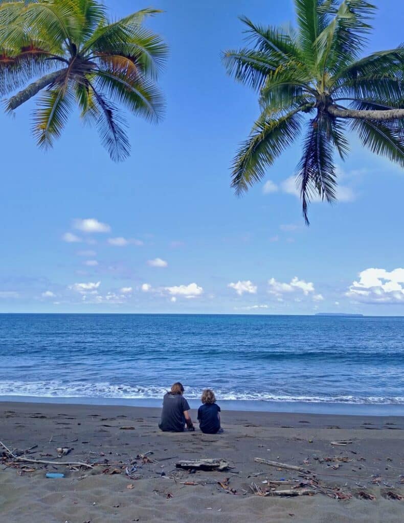 zwei-kinder-sitzen-am-sandstrand-in-costa-rica-unter-palmen
