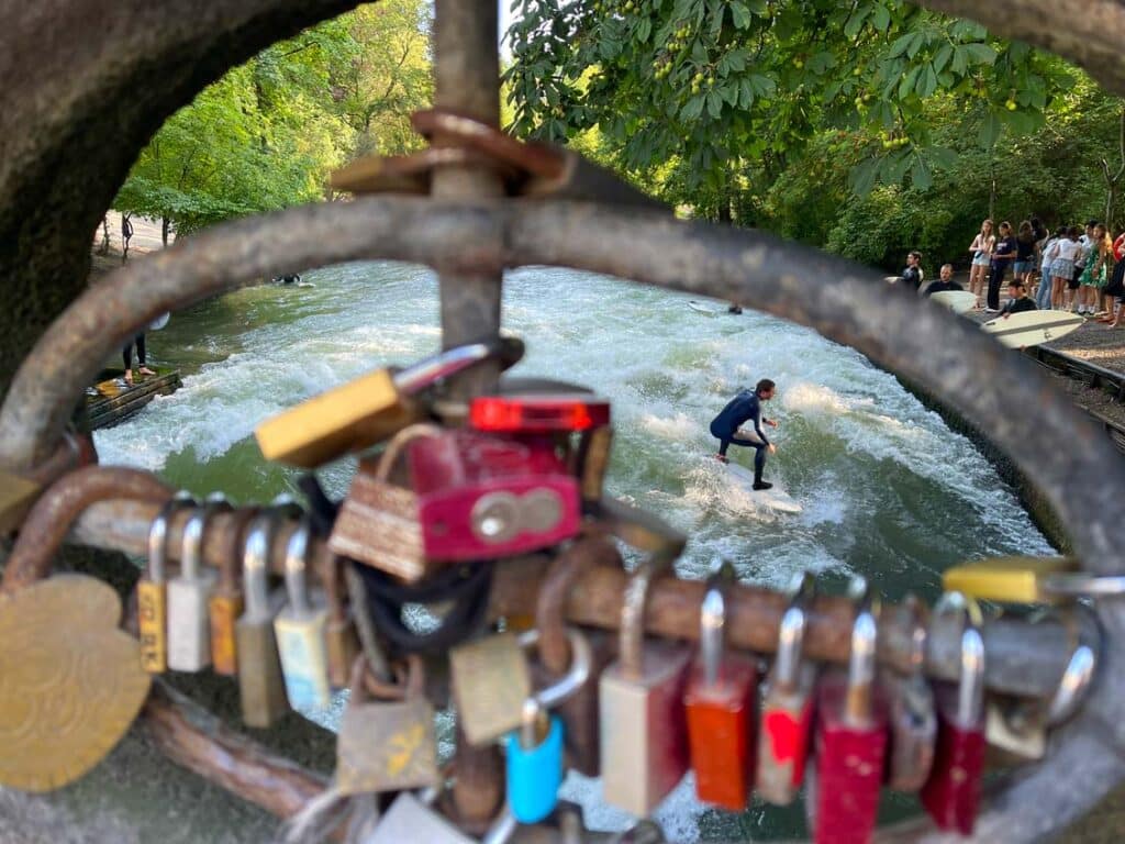 Blick-vorbei-an-Liebesschloessern-auf-surfer-auf-eisbachwelle-im-englischen-garten